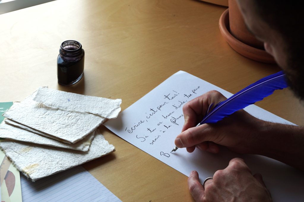 Photo d'une personne écrivant un texte où il est écrit : Écrire, c'est pour toi! Si tu as besoin d'aide, tu peux venir à La Plume.